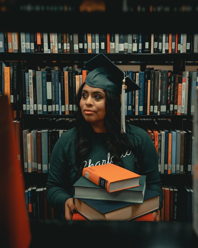 person in academic hat with books